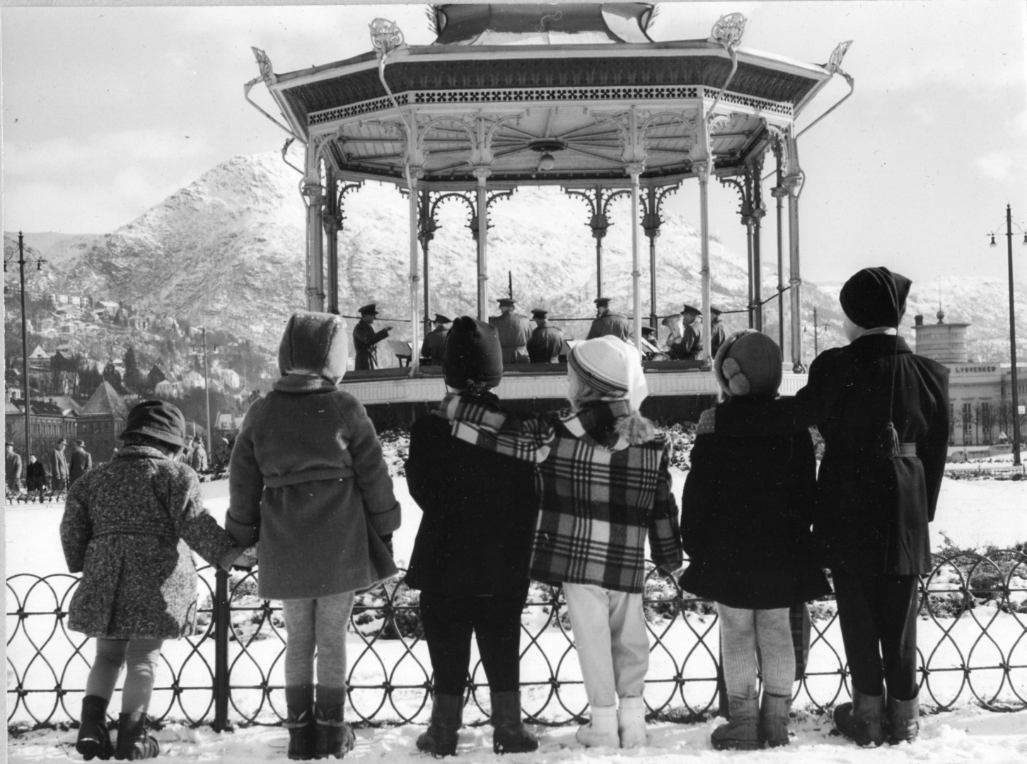 Vi er i 1957, og militærmusikken skal gi Forsvaret et poitivit ansikt i samfunnet. Her spiller Bergenskorpset i Musikkpaviljongen i Bergen sentrum. 