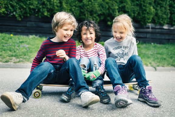 Tre barn sitter på et skateboard og ler