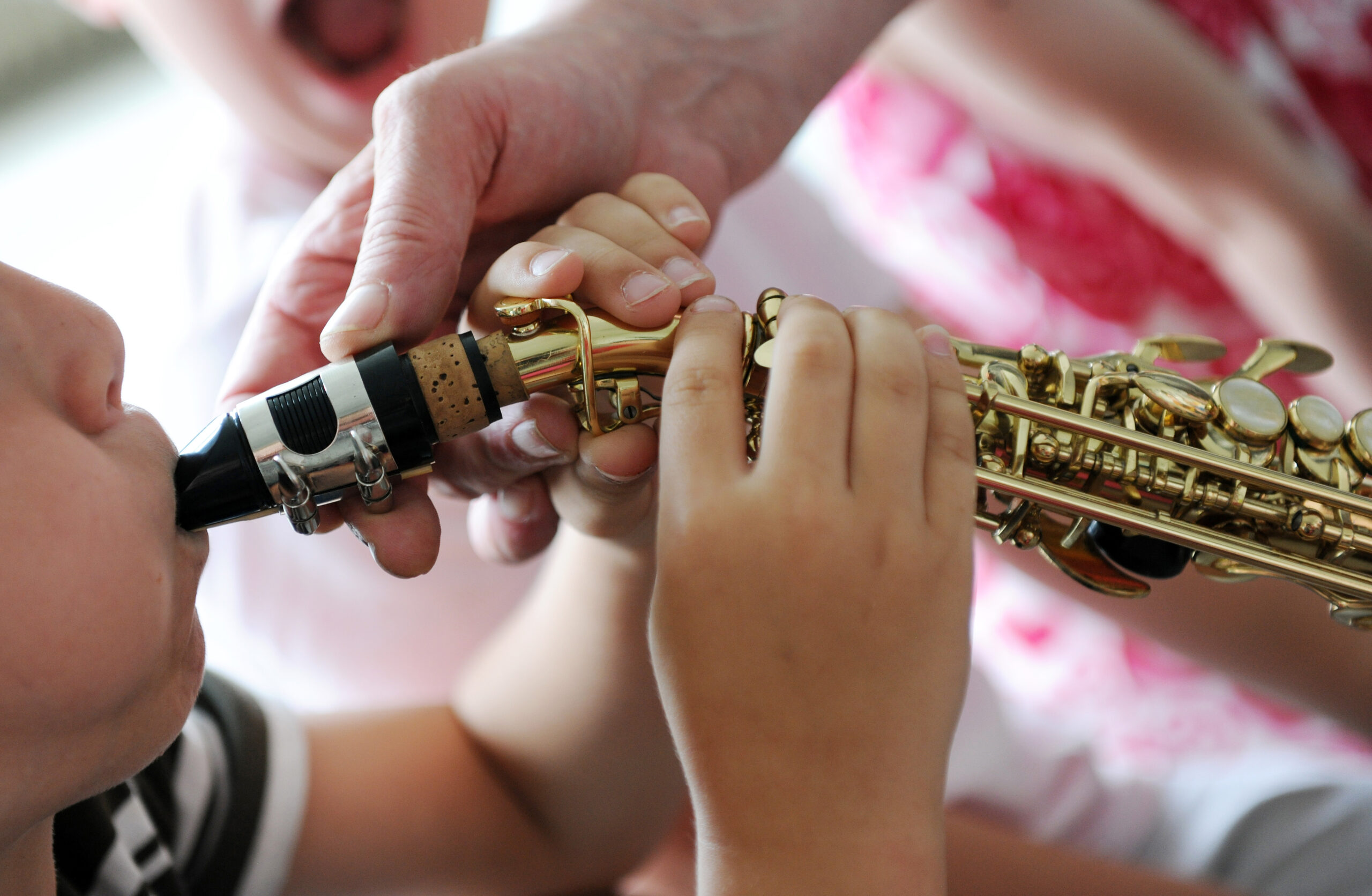 Liten gutt forsøker spille saksofon mens voksen holder i instrumtentet