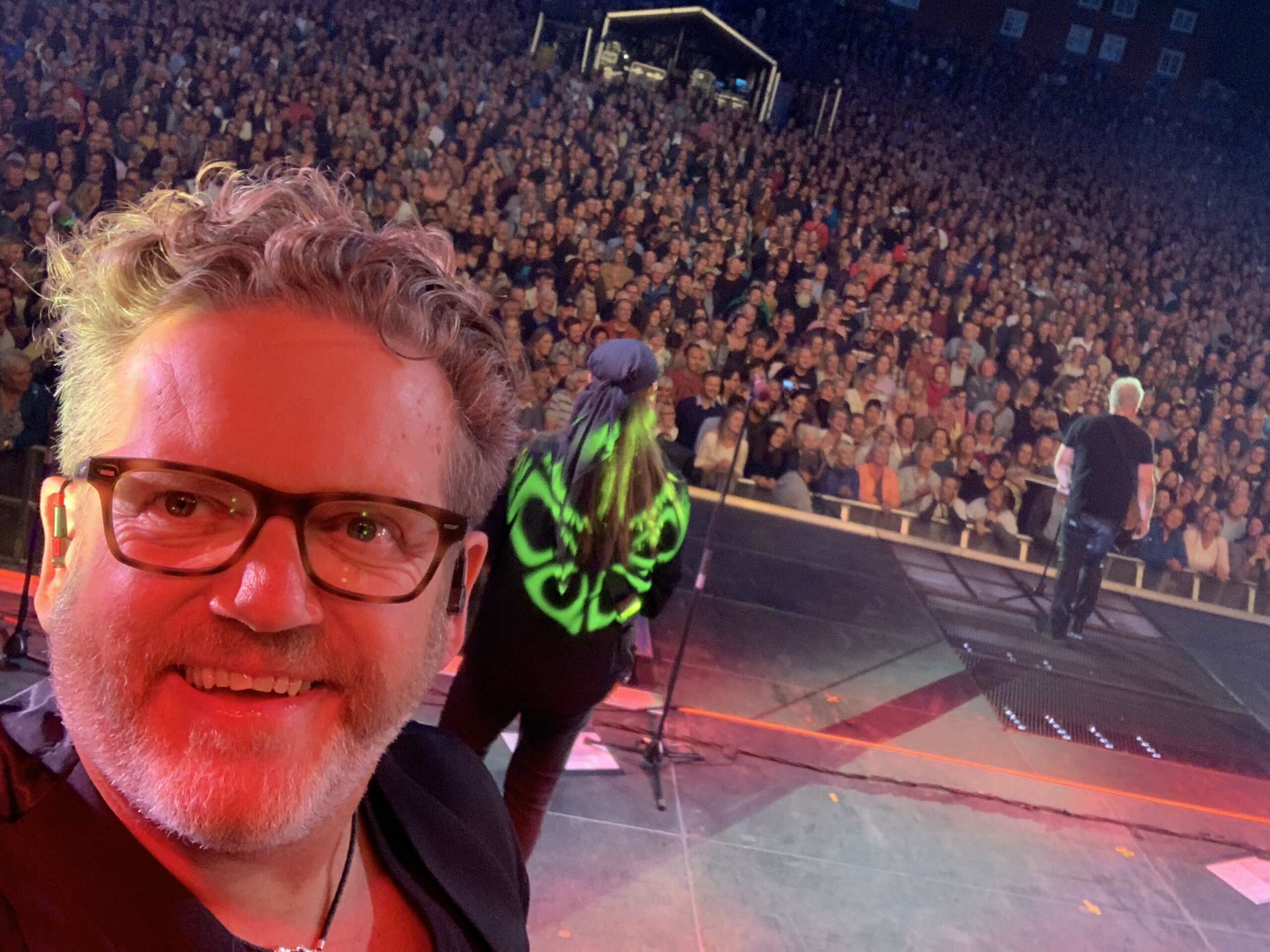 Mann med briller tar selfie på scenen foran stort publikum