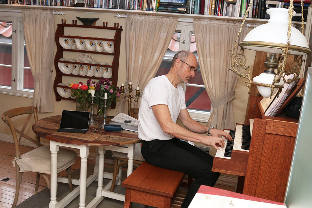 Mann i hvit tskjorte spiller på et orgel i rotete stue