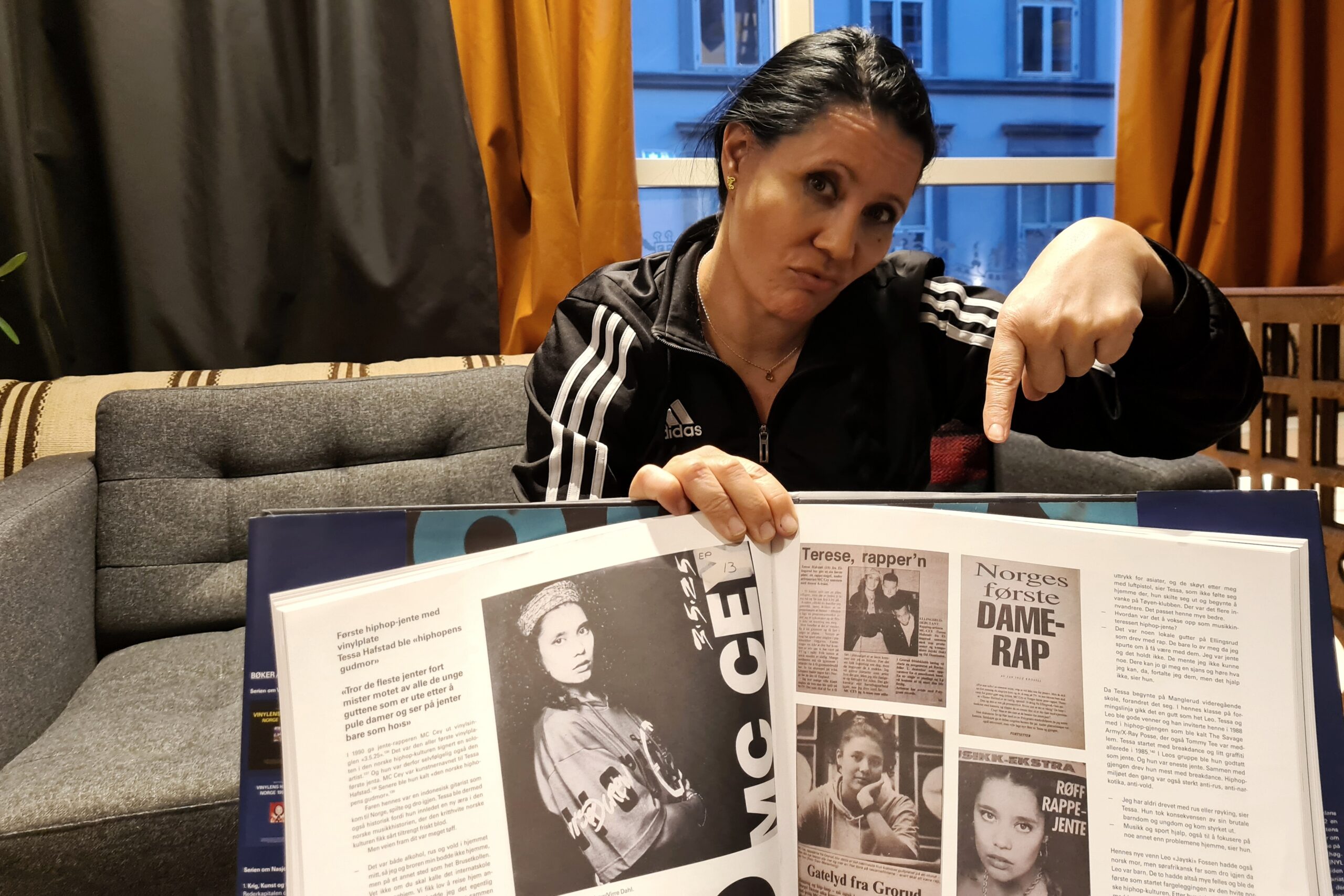 Kvinne holder stor bok og peker ned på gamle bilder av norges første kvinnelige rapstjerne