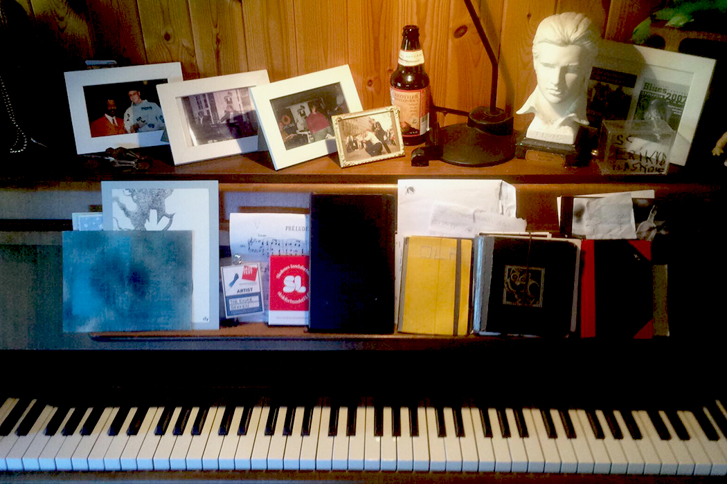 Piano med noter, notatbøker, familiebilder, ølflaske og en byste