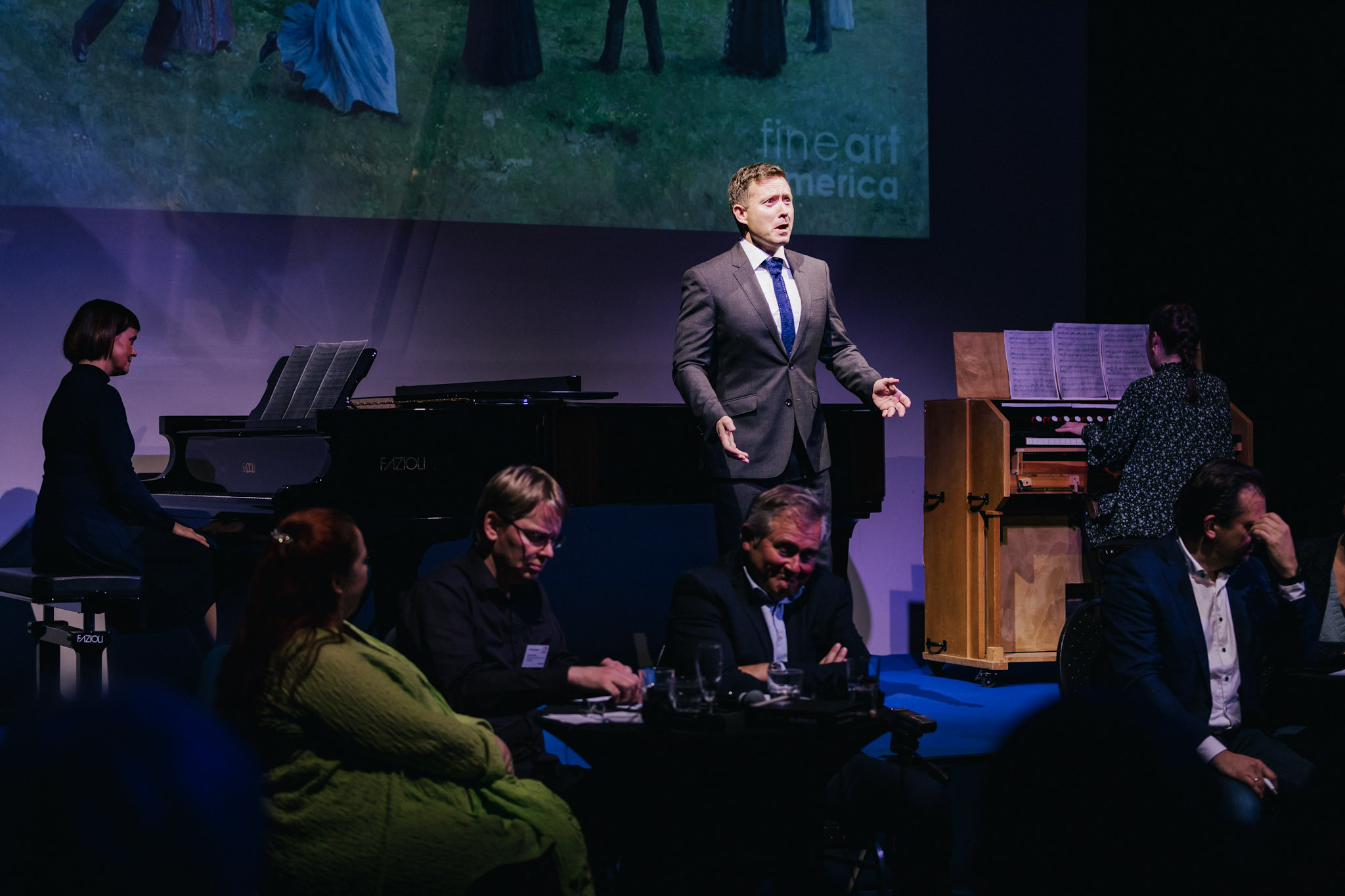 Operasanger i dress på scene med flygel og piano mens folk sitter foran og tenker