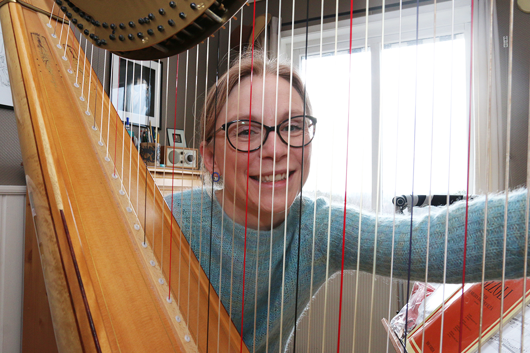 Kvinne med briller bak harpestrenger og harpe i et gjesterom