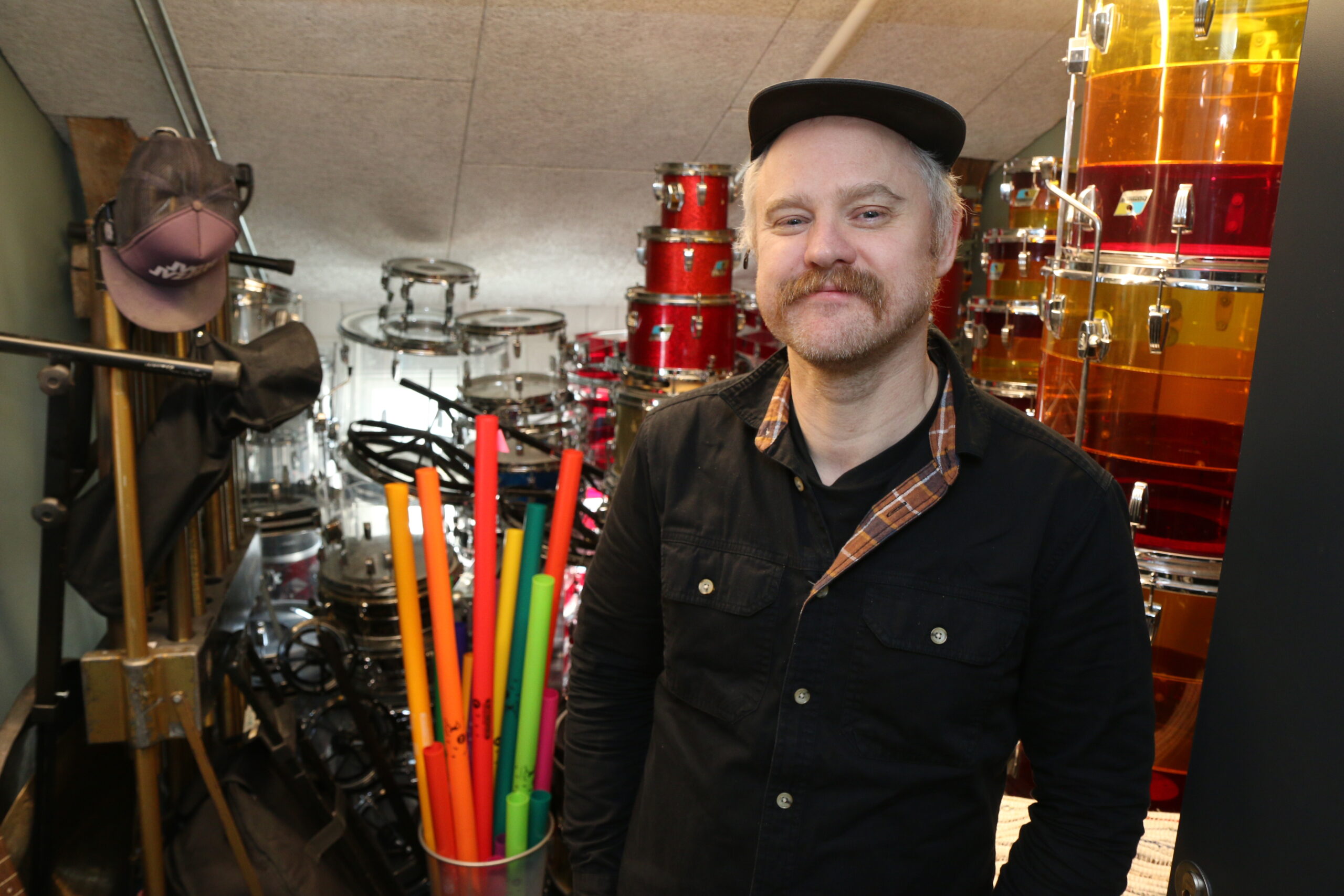 Mann med caps og sort skjorte foran stabler med trommer
