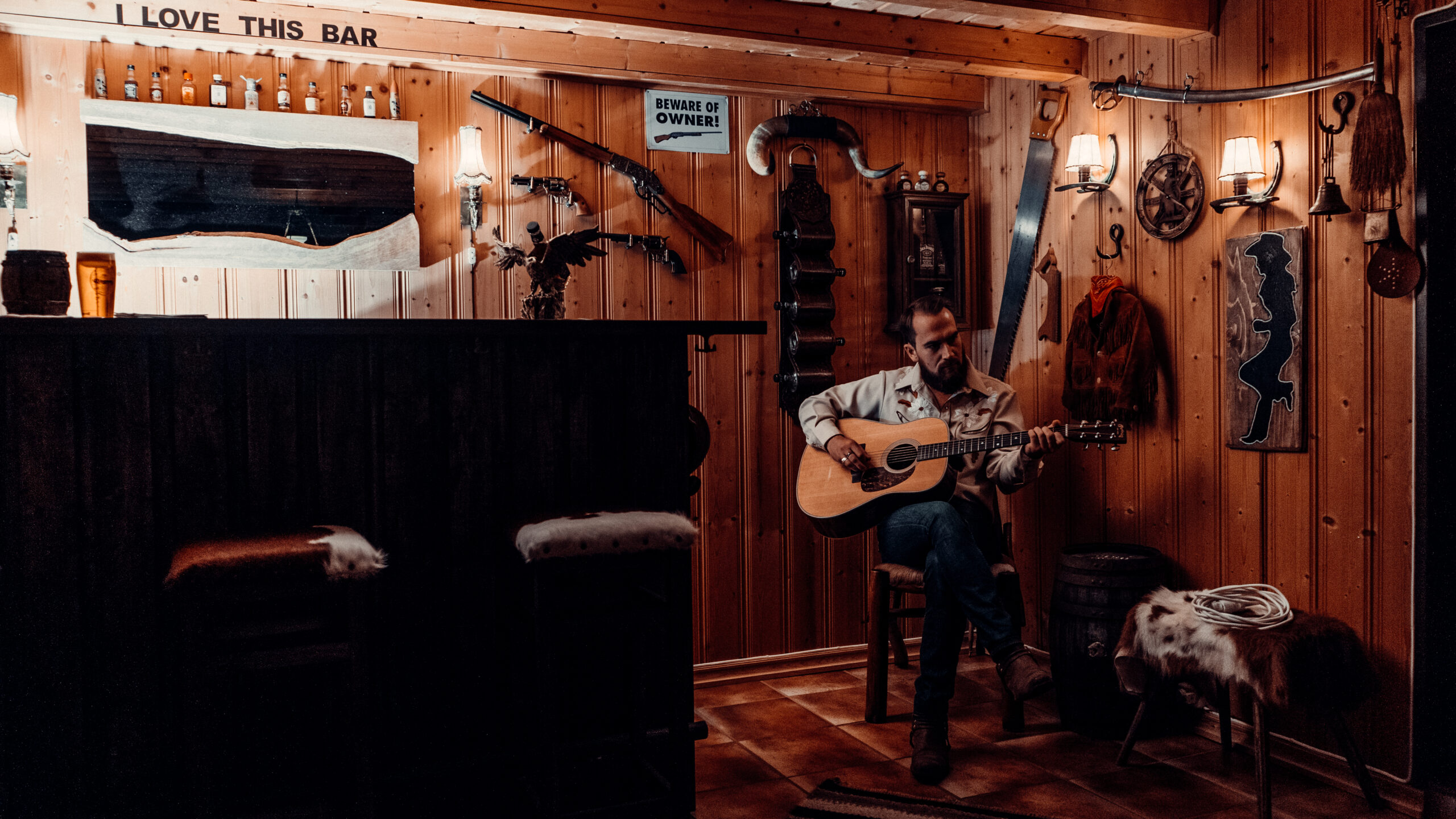 Musiker med gitar, på en krakk i et hjørne på en villmarksbar