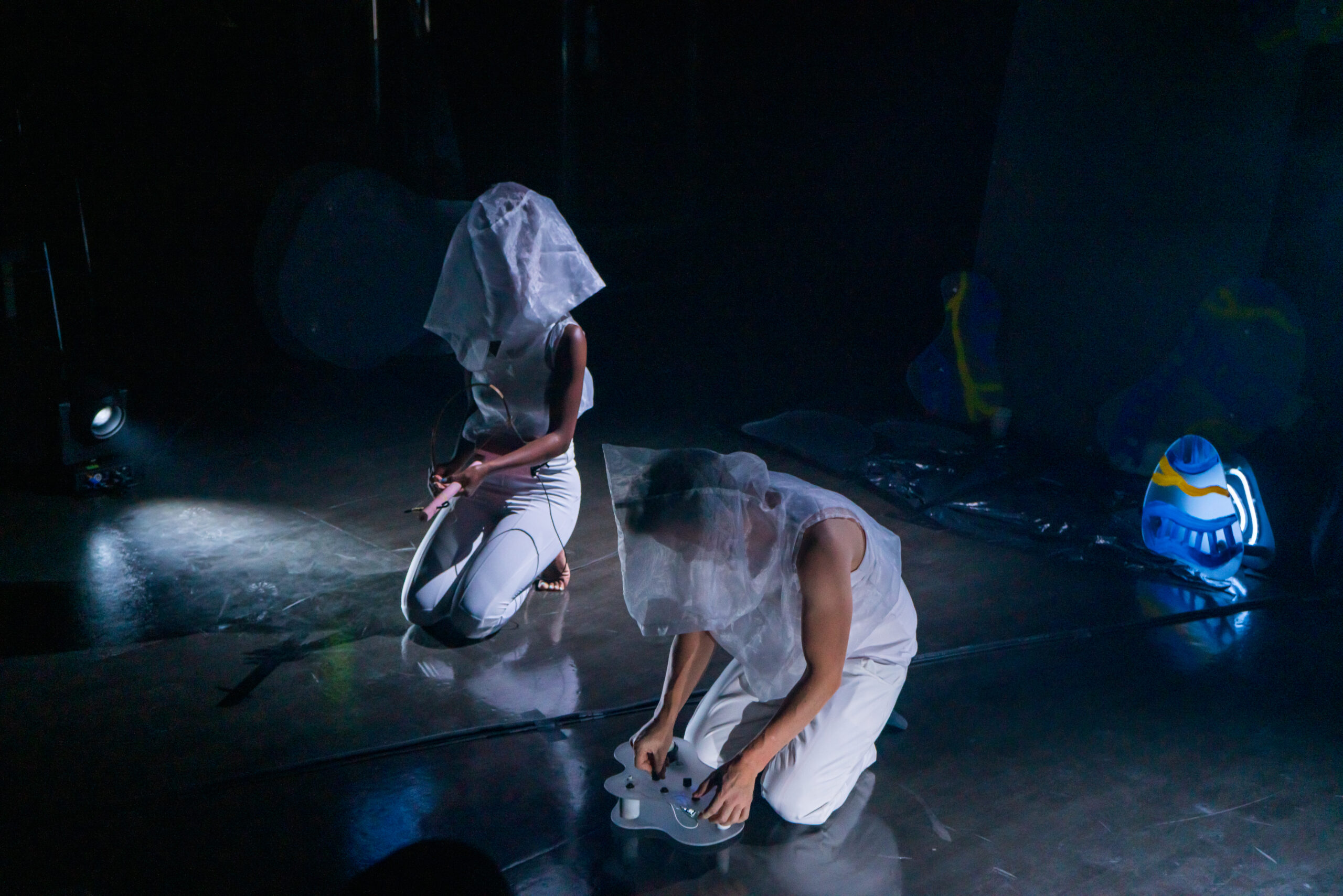 To musikere kledd i hvitt med gjennomsiktig sekk over hodet sitter på en scene
