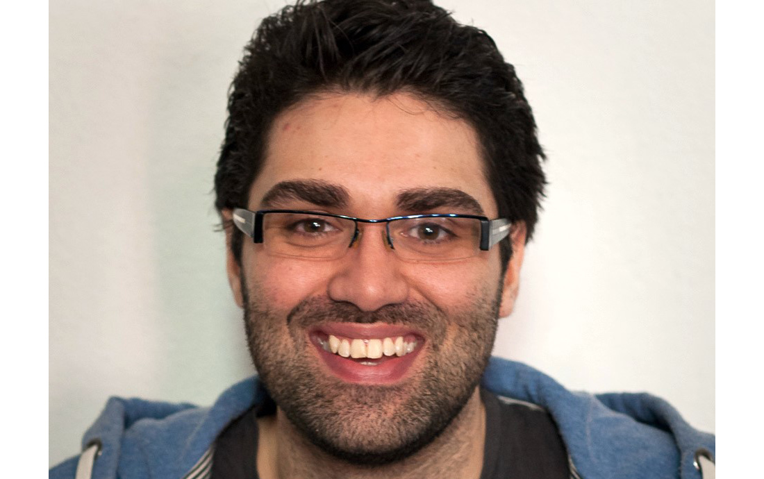 Mann med briller, to-dagersskjedd og kort mørkt hår smiler