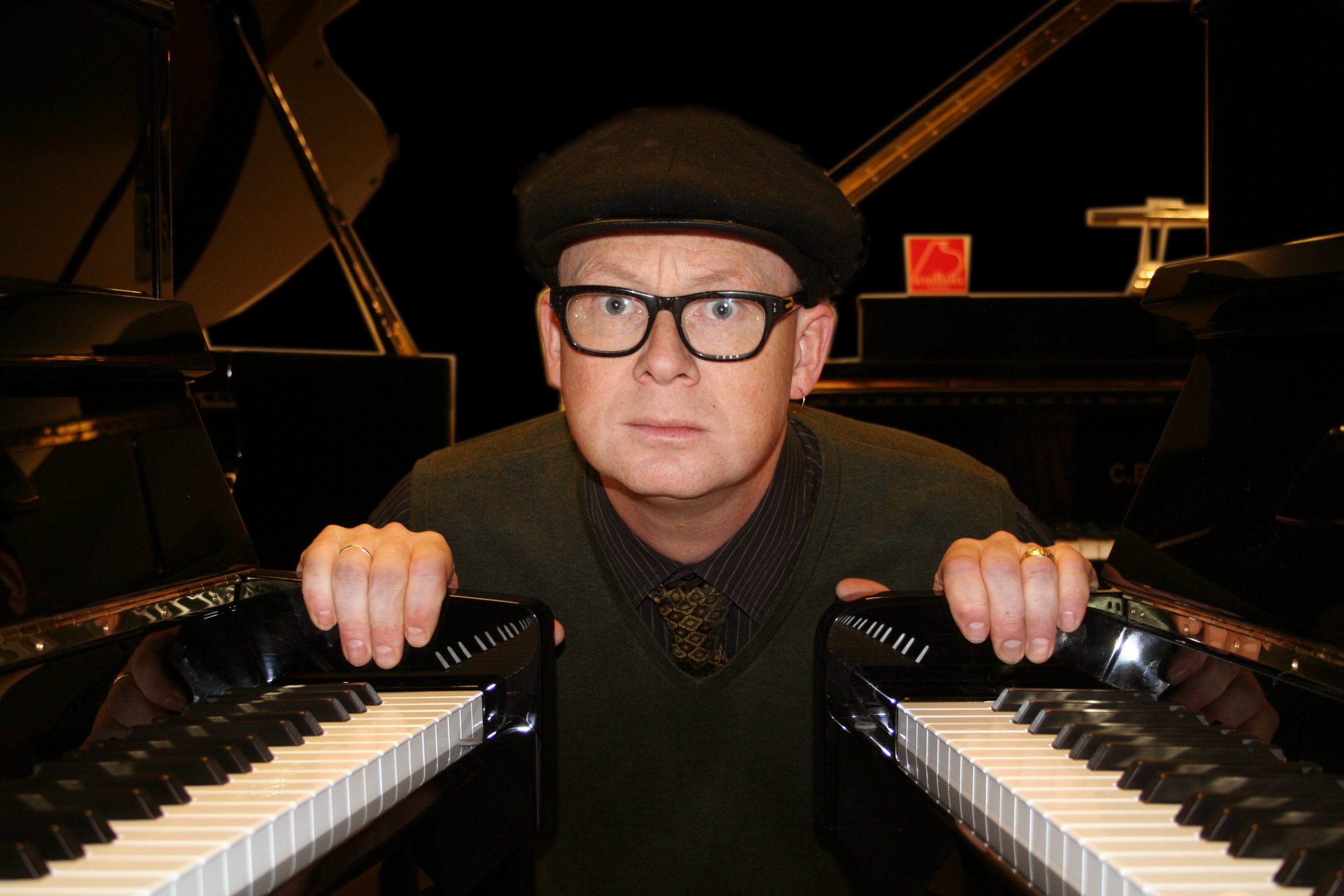 Tor Einar Bekken med hatt og briller i skvis mellom to pianoer
